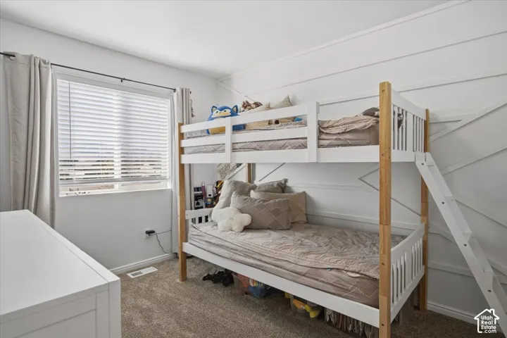 Neutral-toned bedroom featuring white accent wall molding, textured wall-to-wall carpeting, and a double-pane window with hardware for window treatments
