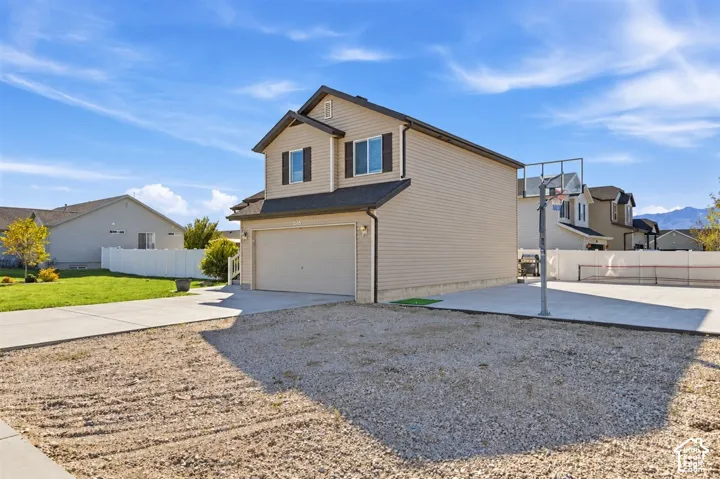 Two-story residence with tan vinyl siding, an attached two-car garage, concrete driveway, and a gravel front yard