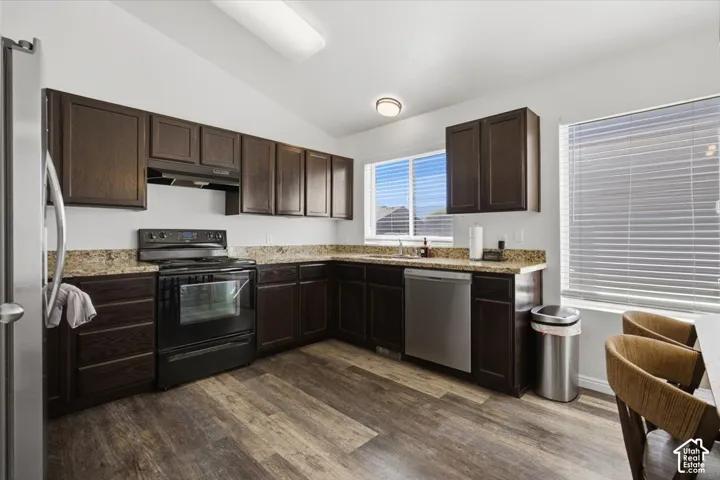 Kitchen featuring dark wood-finish cabinetry, stone-style countertops, stainless steel appliances, and wood-finish flooring