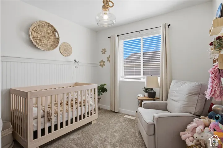 Beadboard wainscoting, neutral carpeting, window with horizontal blinds, and a decorative pendant fixture with a rope-wrapped cord