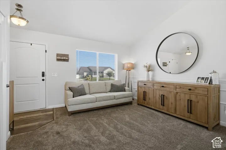 Interior room featuring vaulted ceilings, decorative wainscoting, a large picture window, and multi-tone flooring with wood-finish entry and carpeted living area