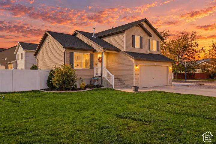 Two-story residence featuring light-colored horizontal siding, an attached two-car garage, white vinyl fencing, and a concrete driveway
