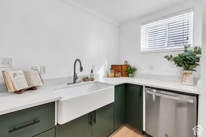 Custom dark green cabinetry featuring matte black hardware, white stone-finish countertops, an undermount farmhouse sink, a gooseneck faucet, and a stainless steel dishwasher