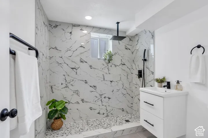 Walk-in shower featuring floor-to-ceiling large-format tile with marble-patterned finish, pebble-stone flooring, matte black rainfall showerhead, and a modern floating vanity