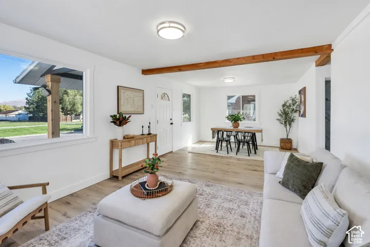 Living area featuring wood-finish flooring, exposed wood ceiling beams, neutral wall tones, and flush-mount lighting fixtures