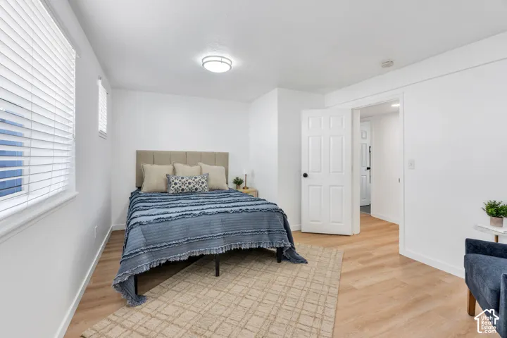 Neutral-toned room featuring wood-finish flooring, white walls, horizontal blinds, and a flush-mount ceiling light fixture with a six-panel door
