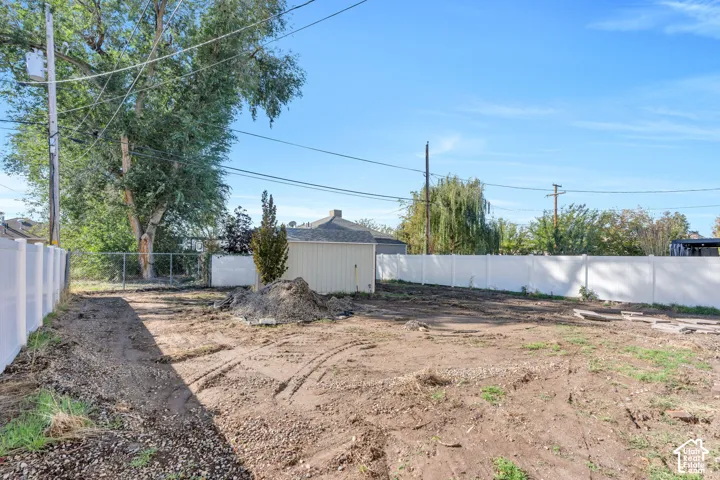 Spacious backyard enclosed by solid white vinyl fencing, featuring a detached storage structure and mature trees