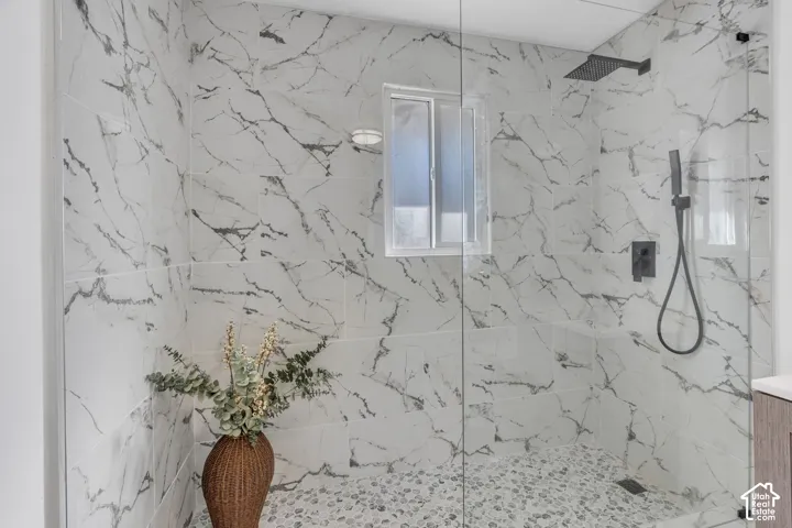 Walk-in shower featuring large-format patterned wall tile, pebble-style floor tile, a frameless glass enclosure, and matte black plumbing fixtures