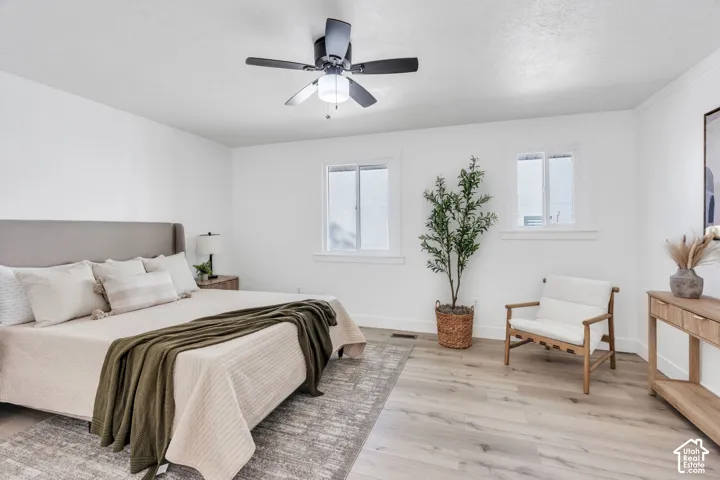 Neutral-toned interior featuring wood-finish flooring, two windows with white trim, and a ceiling-mounted light fixture with a fan