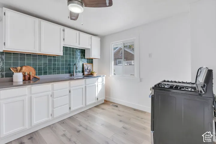 Kitchen featuring white shaker-style cabinetry, dark solid-surface countertops, green ceramic tile backsplash, wood-finish flooring, and a ceiling-mounted light fixture with integrated fan