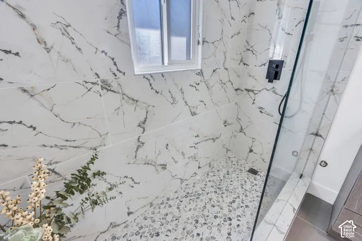 Walk-in shower featuring large-format veined tile wall surrounds, river rock flooring, a glass enclosure, and matte black plumbing fixtures