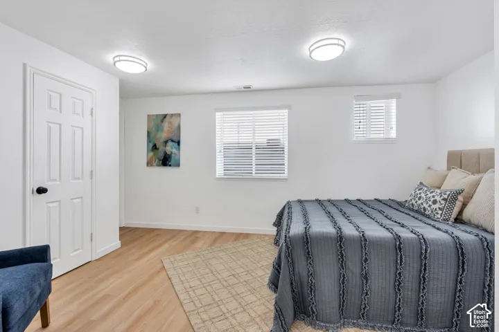 Neutral-toned room featuring wood-finish flooring, two flush-mount ceiling light fixtures, two windows with horizontal blinds, and a paneled interior door