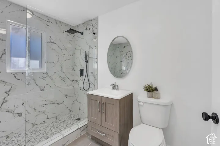 Bathroom featuring a walk-in shower with stone-patterned wall tile, pebble-tile flooring, and matte black fixtures, paired with a wood-finish vanity and oval mirror