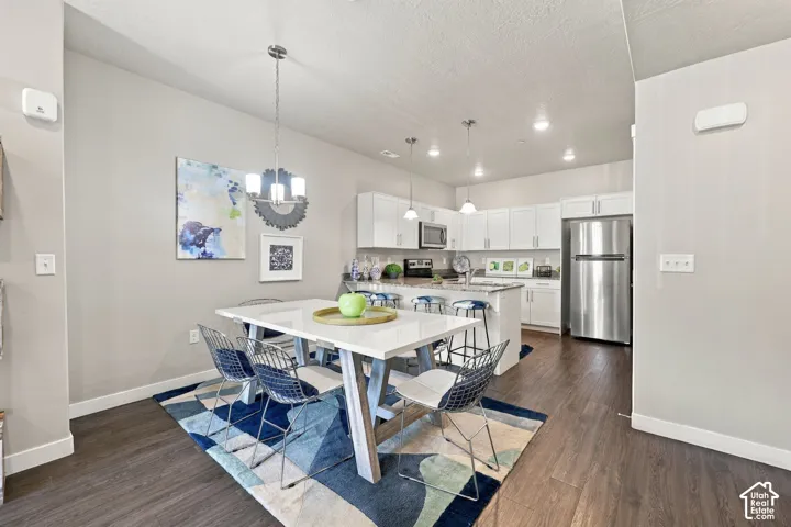 Kitchen featuring white cabinetry, stone-surface countertops, stainless steel appliances, and wood-finish flooring, illuminated by pendant lighting
