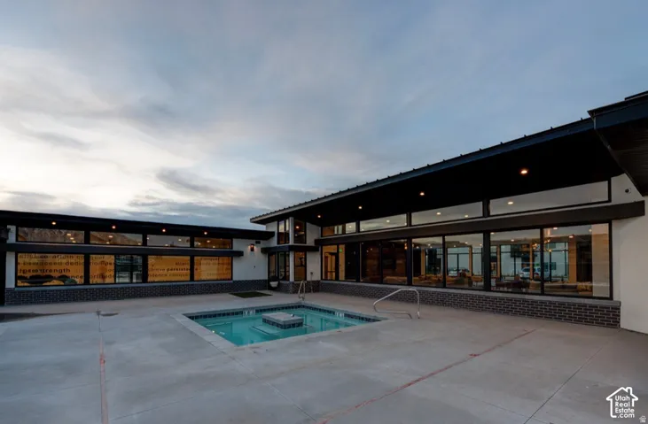 Modern exterior featuring extensive floor-to-ceiling glass paneling, dark masonry wainscoting, a concrete patio, and an in-ground spa