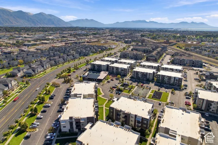 Aerial perspective of the residential complex featuring flat-roofed multi-story structures, dedicated surface parking, outdoor recreational spaces, manicured green space, and a mountainous backdrop