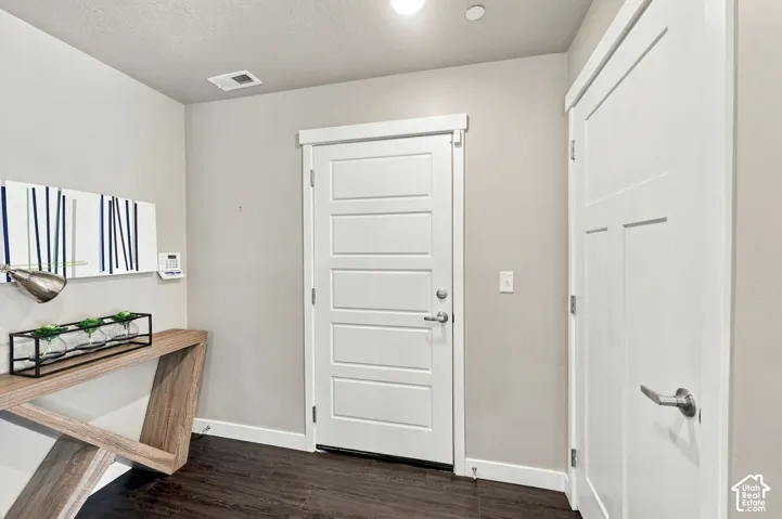 Entryway featuring dark wood-finish flooring, a white five-panel interior door, and a matching white shaker-style door with brushed metal hardware