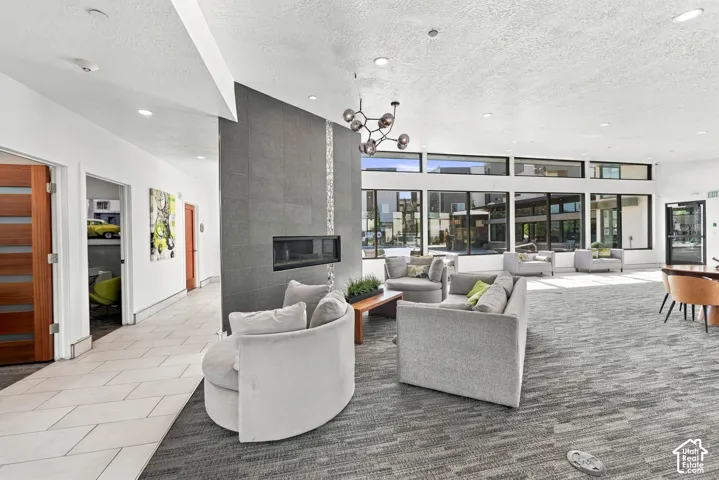 Floor-to-ceiling windows, dual-sided fireplace with dark stone surround, recessed lighting, modern multi-arm chandelier, and tiled flooring