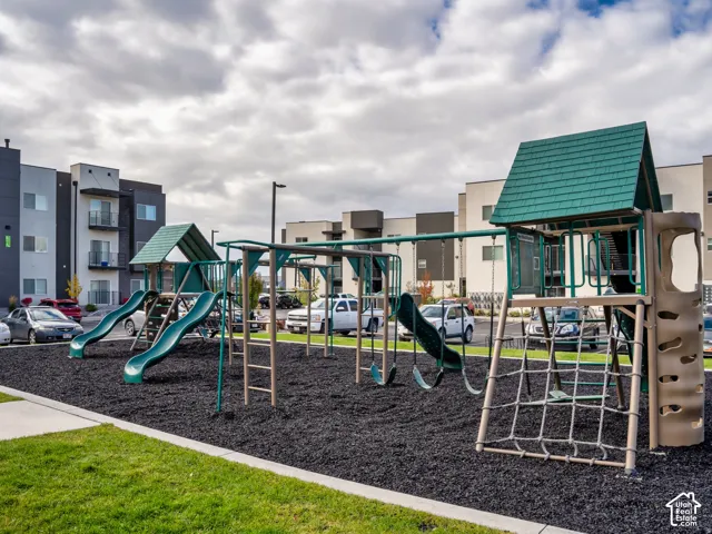 Outdoor play area featuring multi-level climbing structures, green shingled roofs, integrated slides, and a rope climbing net set within a rubberized mulch surface