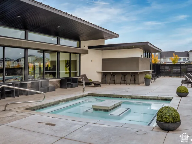 In-ground spa featuring a concrete surround and built-in entry steps, complemented by an outdoor bar area with a stone-top counter and expansive floor-to-ceiling windows
