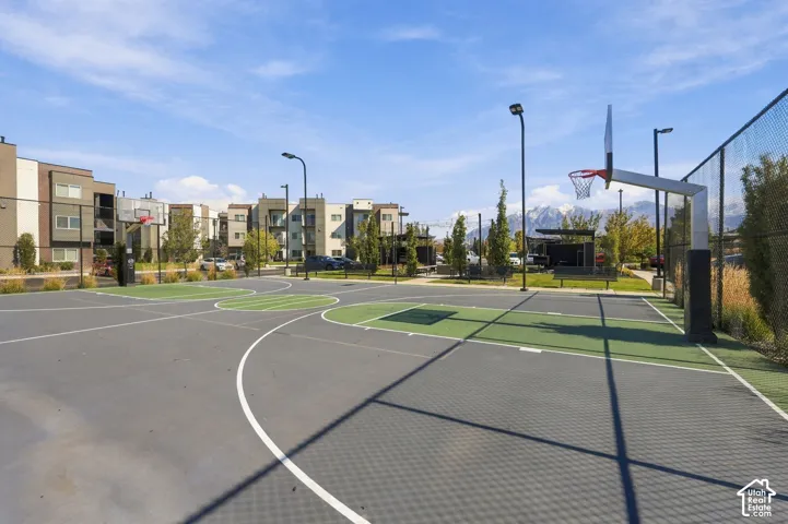 Outdoor basketball court featuring multi-colored hardscaping, chain-link fencing, dual hoops, and pole-mounted lighting