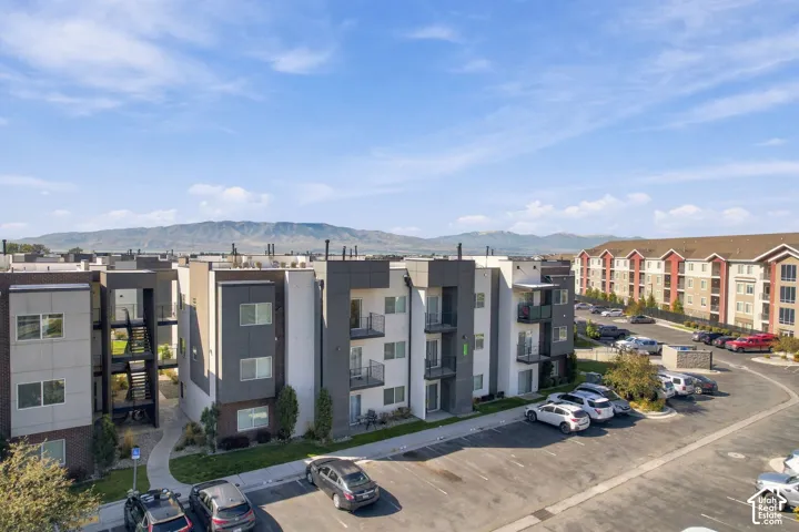Multi-story residential complex featuring contemporary stucco and masonry facade, private balconies, asphalt parking, and mountain scenery