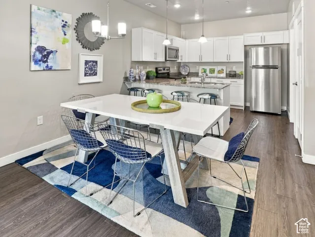 Kitchen featuring white shaker-style cabinetry, a stone-surfaced island with bar seating, stainless steel appliances, and wood-finish flooring