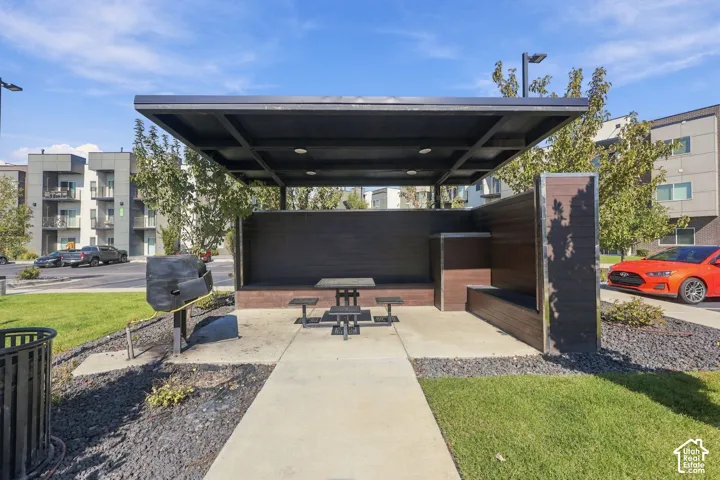 Outdoor pavilion featuring a modern flat-roof structure, built-in wooden bench seating, integrated recessed lighting, and a dedicated grilling area