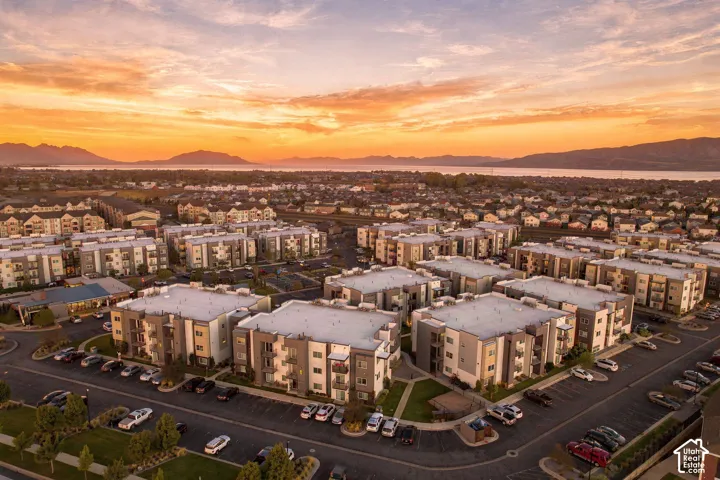 Aerial perspective of a multi-unit residential complex featuring flat-roof architecture, asphalt parking areas, integrated landscaping, and a mountain and lake backdrop