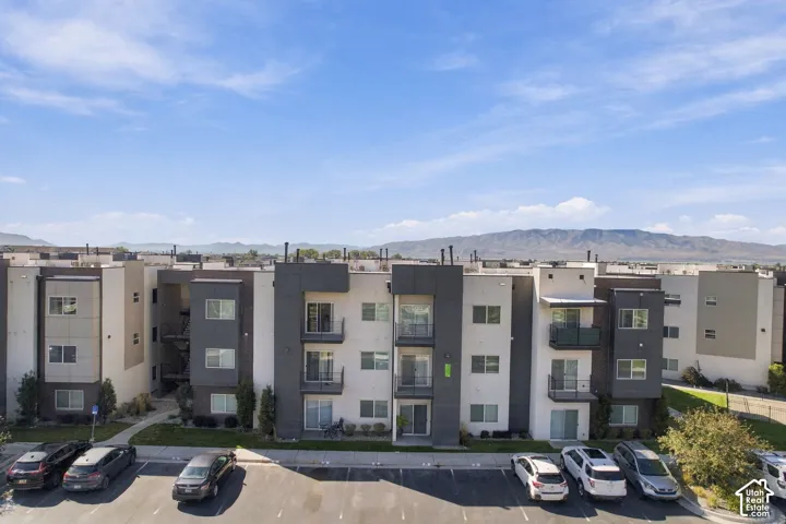 Multi-story residential building featuring a modern stucco exterior, private recessed balconies with dark metal railings, and mountain scenery