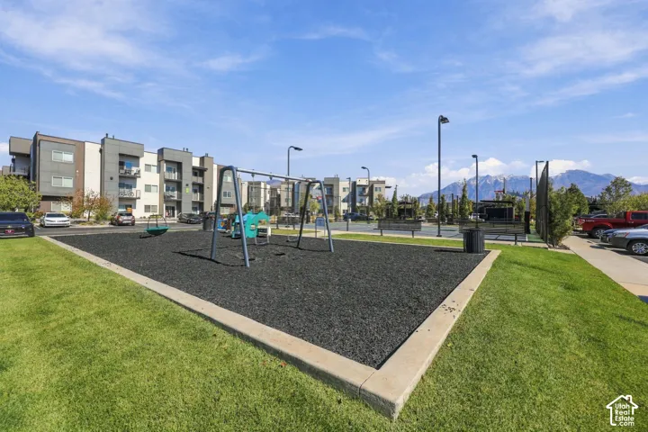 Common area featuring a playground with a rubberized surface, manicured lawn, outdoor lighting, and mountain backdrop