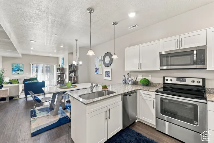 Kitchen featuring white shaker-style cabinetry, stone-surface countertops, stainless steel appliances, an undermount sink, and pendant lighting