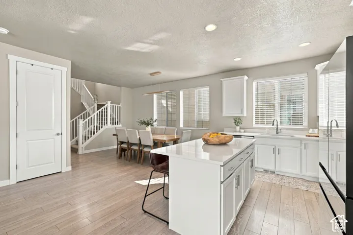 Kitchen featuring a central island with a solid-surface countertop, white shaker-style cabinetry, recessed lighting, and wood-finish flooring