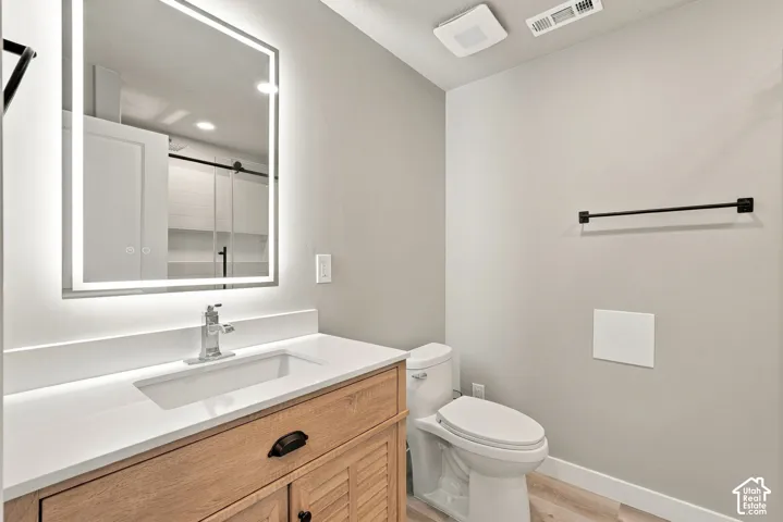 Bathroom featuring a wood-finish vanity with louvered cabinet doors, a rectangular undermount sink, quartz countertop, and a backlit LED mirror with matte black hardware