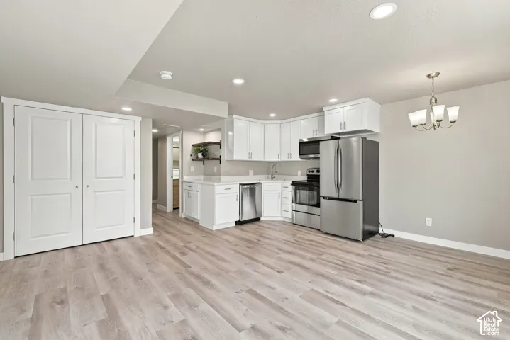 Kitchen featuring white cabinetry, wood-finish flooring, stainless steel appliances, recessed lighting, and a multi-arm chandelier