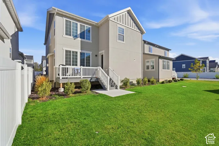 Rear exterior featuring multi-level siding, a raised deck with white railings, a concrete landing, and a grass yard enclosed by a vinyl fence