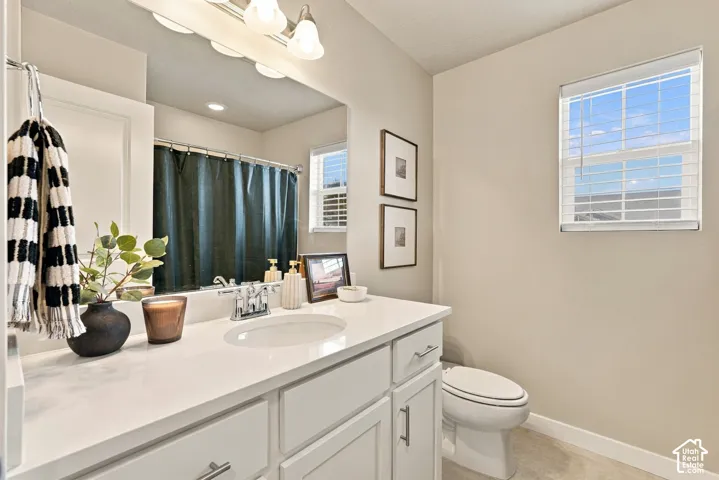 Bathroom featuring a vanity with white cabinetry, a light-toned countertop, an integrated oval basin, a multi-bulb light fixture, and a window with blinds