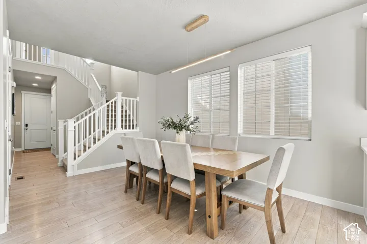 Dining area featuring wood-finish flooring, dual windows with blinds, a linear pendant light fixture, and a staircase with white balusters