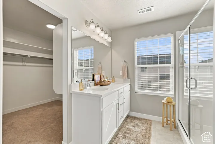 Dual-sink vanity with white cabinetry and solid-surface countertop, full-width vanity mirror, five-light fixture, glass-enclosed shower, and walk-in closet with built-in shelving