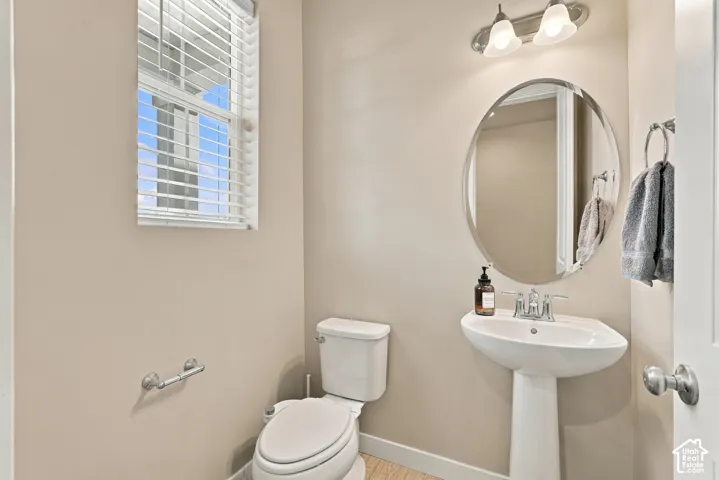 Powder room featuring a pedestal sink, polished chrome widespread faucet, oval wall-mounted mirror, two-light fixture, and horizontal blind window covering
