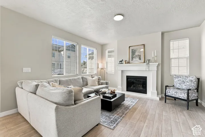 Living area featuring wood-finish flooring, white fireplace mantel, gas insert, and multiple windows with horizontal blinds