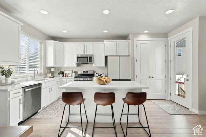 Kitchen featuring white shaker-style cabinetry, quartz countertops, central island, stainless steel appliances, and wood-finish flooring