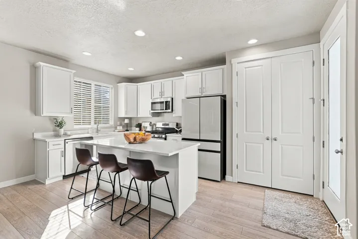 Kitchen featuring white shaker-style cabinetry, quartz countertops, a center island with bar seating, stainless steel appliances, and wood-finish flooring