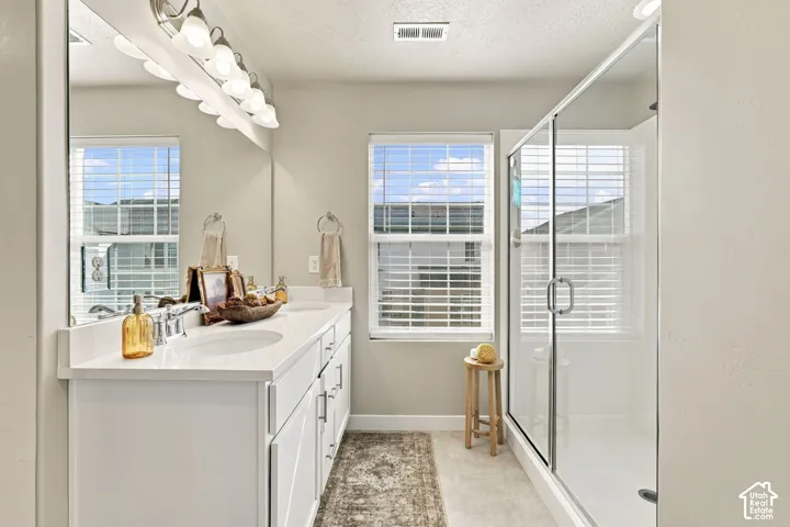 Dual-sink vanity with a solid-surface countertop, full-width mirror, glass-enclosed shower, and multi-bulb overhead vanity lighting