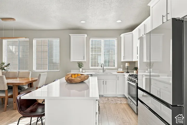 Kitchen featuring a central island with a solid surface countertop, white shaker-style cabinetry, stainless steel appliance suite, and wood-finish flooring