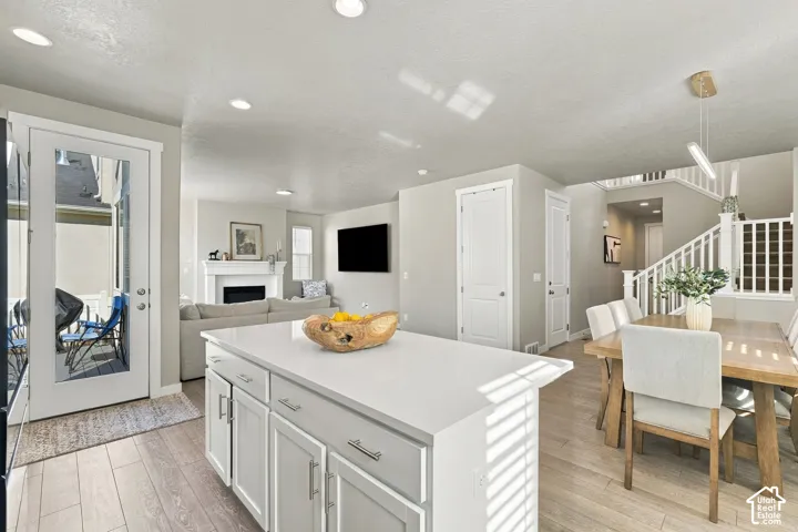 Kitchen island with a solid-surface countertop and shaker-style cabinetry, complemented by wood-finish flooring, recessed lighting, and a fireplace with a decorative mantel