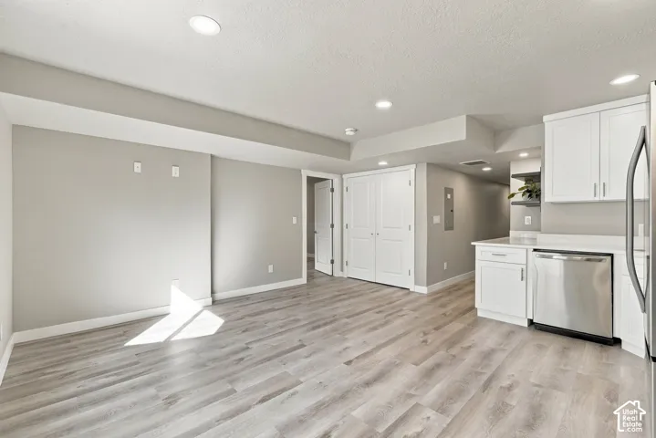 Open-concept area featuring wood-finish flooring, recessed lighting, white cabinetry, and stainless steel kitchen appliances