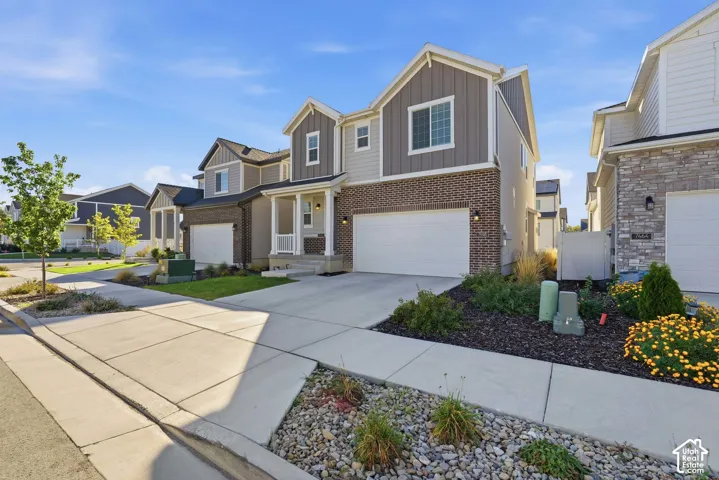 Two-story residence featuring a brick and vertical siding exterior, attached two-car garage, covered entryway, and landscaped front yard