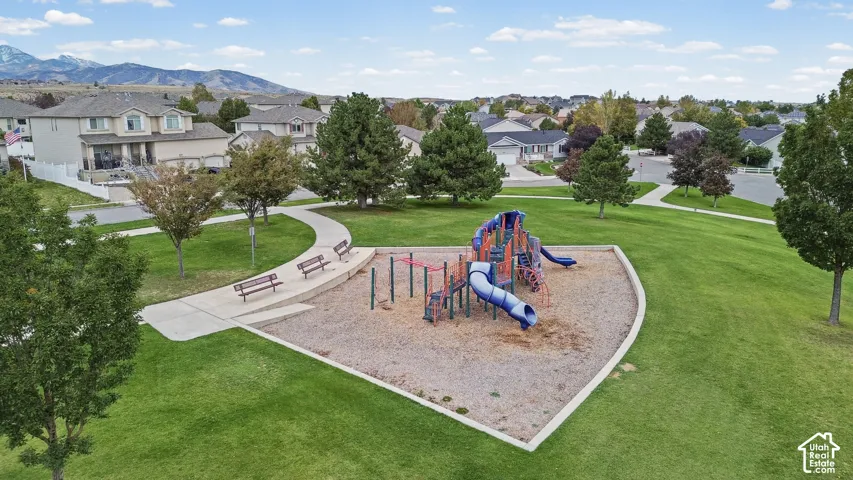 Community park space featuring a playground with a slide, paved walkways, integrated benches, manicured lawn, and mature trees with a mountain backdrop