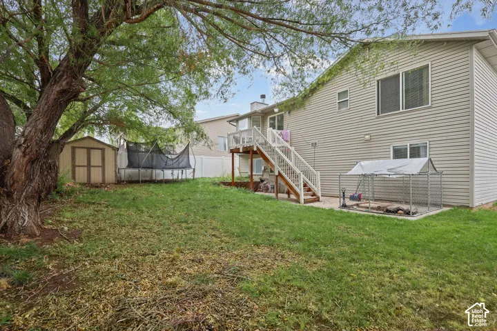 Rear exterior featuring vinyl siding, an elevated wood deck with stairs, a detached storage shed, and white vinyl perimeter fencing